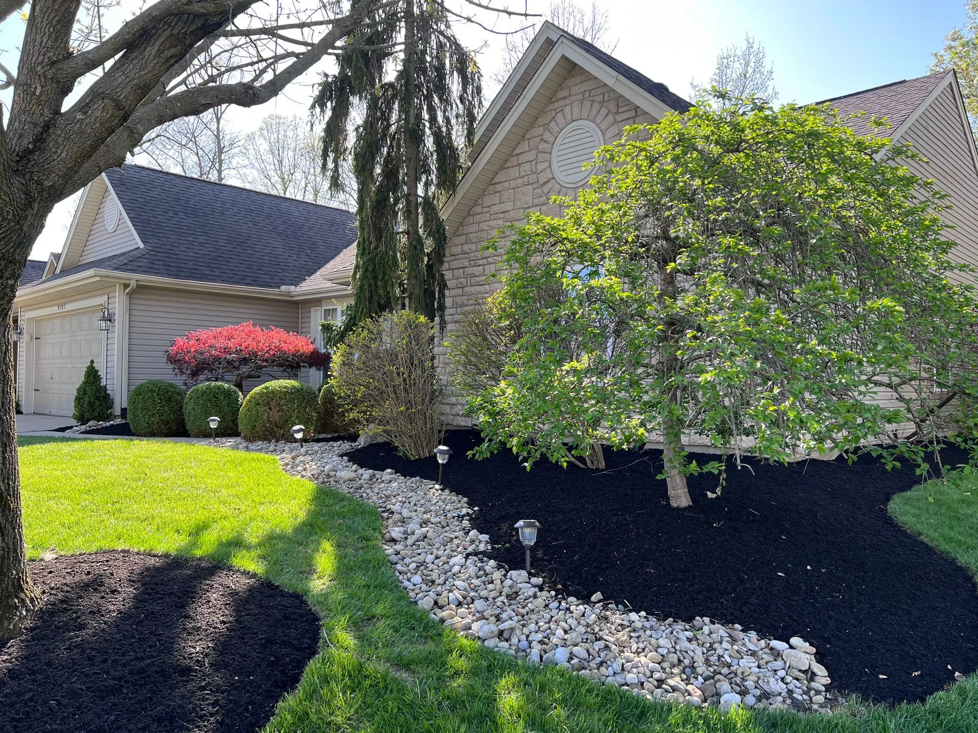 Front-yard landscaping with fresh black mulch beds and a river-rock border